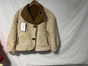 Détail d'une veste en polaire beige avec col et bordures marron sur un cintre en bois