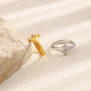 Close-up of gold and silver four-pointed star rings with zircons on a natural stone