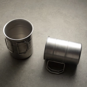 Outdoor camping 304 stainless steel cups with portable folding handles on concrete surface
