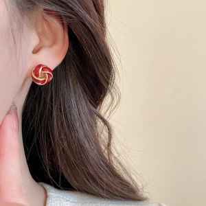 Close-up of red enamel knot stud earring with golden metal weave on female model