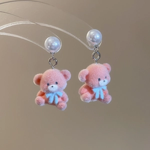 Detailed macro shot of pink flocked bear earrings with a blue bow and white pearl stud