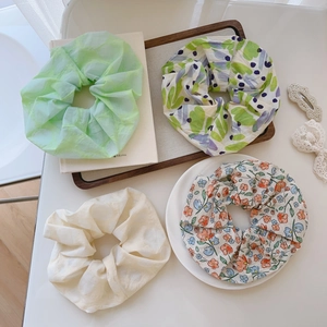 Set of four floral and pleated chiffon hair scrunchies on a minimalist white desk