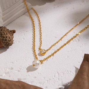 Detail of gold double-layer necklace with pearl and zircon pendant on a white texture