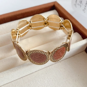 Macro detail of golden oval bracelet links with red rose relief and enamel inlay