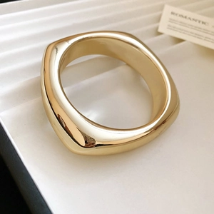 Gros plan sur un large bracelet jonc doré ajouré avec un design carré métallique