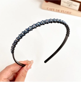 Detail of a slim black headband with sparkling blue rhinestone flowers on a clean white surface