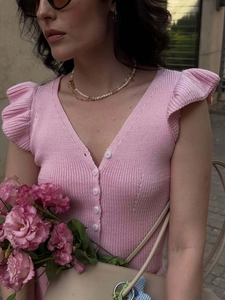 Detail of pink knit top featuring delicate ruffle sleeves and elegant white front buttons