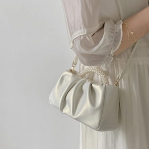 Detailed view of white pleated cloud bag with pearl handle and slim crossbody strap