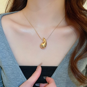 Close-up of a minimalist golden water drop pendant necklace worn by a model in natural light