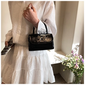 Dettaglio borsa in pelle verniciata nera con elegante decoro fiocco in metallo