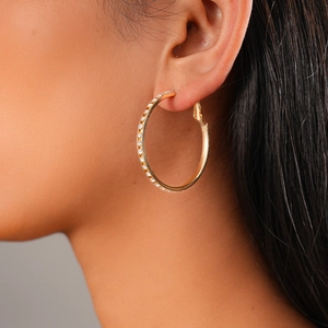 Close-up of a large gold hoop earring with pavé white zircon stones on a female model