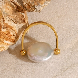 Détail macro d'une perle baroque sur une bague dorée en U sur fond de pierre
