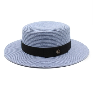 Vue détaillée du ruban noir et du logo M doré sur un chapeau de paille de canotier bleu