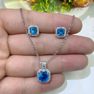 Detail of hand holding a blue zircon octagonal pendant necklace and stud earrings set