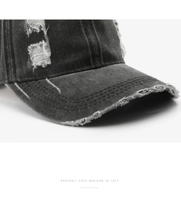 Close-up of distressed black denim baseball cap featuring vintage washed ripped details