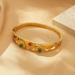 Detailed macro of gold-plated evil eye bangle with colorful stones on satin background