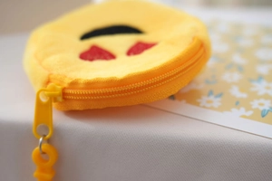 Close-up of yellow plush coin purse with heart eye emoji embroidery and matching zipper