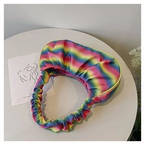 Top view of a pleated rainbow gradient shoulder bag on a minimalist white table setting