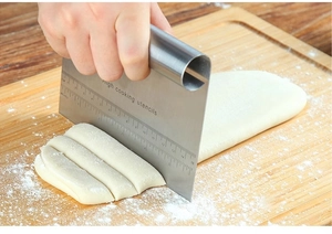 Close-up of stainless steel dough scraper with measurements cutting dough on wood