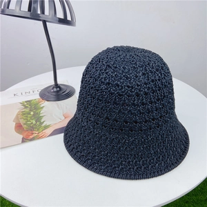 Detailed view of black hollow-knit straw bucket hat on a white table with a magazine