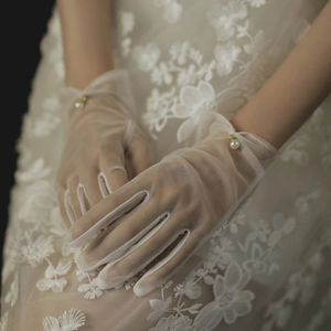 Close-up of white sheer bridal gloves with elegant pearl accents on wrist and lace details