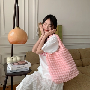 Close-up of pink popcorn texture shoulder bag held by a model in a cozy indoor setting