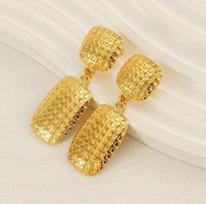 Detail of gold square checkered stud earrings on white textured background