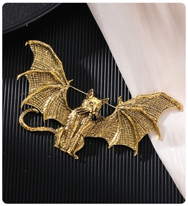 Detailed close-up of a vintage gold bat cat brooch with wings on silk fabric