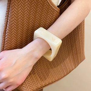 Detail of cream white resin square bangle with cloud texture worn on a woman's wrist