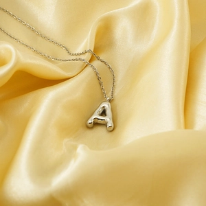 Polished silver bubble initial A pendant necklace on golden silk fabric background