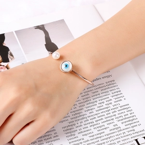 Detail of rose gold evil eye bracelet with white pearl on a fashion magazine background