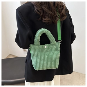 Close-up of green corduroy bucket bag worn crossbody, showing soft texture and strap detail