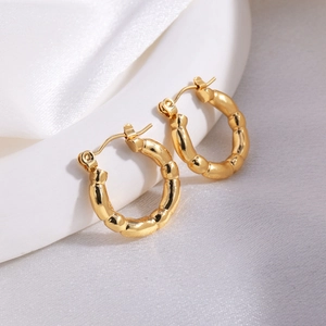 Close-up of gold bamboo-style hoop earrings on a white minimalist display stand