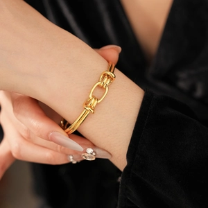 Detailed view of a gold-plated oval knot cuff bracelet worn on a model's wrist