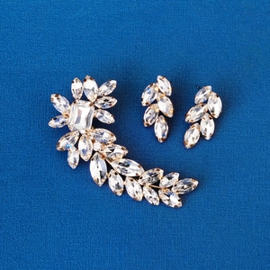 Detailed close-up of gold leaf-shaped crystal ear cuff set on a blue textured surface