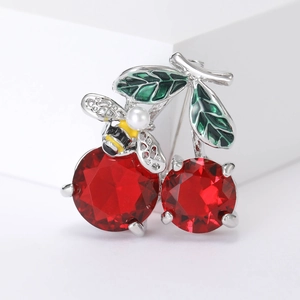 Detail of crystal cherry brooch with red gemstones, green leaves and a pearl bee accent