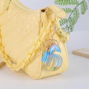 Blue ocean mermaid tail letter D keychain with tassel hanging on a yellow quilted bag