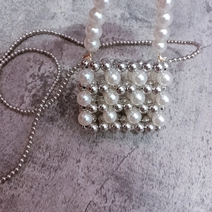 Detailed close-up of woven silver beads and white pearls on a mini crossbody bag