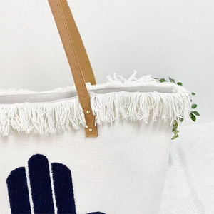Close-up of bohemian canvas tote with fringe trim, blue flocking, and brown leather handles