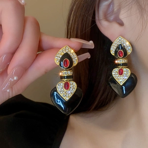Detail of vintage heart earrings with black enamel, red gems and gold metal plating