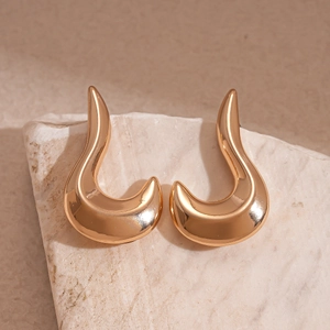 Macro detail of abstract curved gold metal earrings on natural stone surface