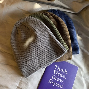 Multiple vintage knitted beanies in grey, green, brown, and navy on a fabric background