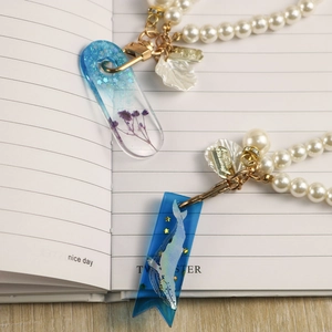 Detail of DIY resin bookmarks with dried flowers and whale patterns on a white notebook