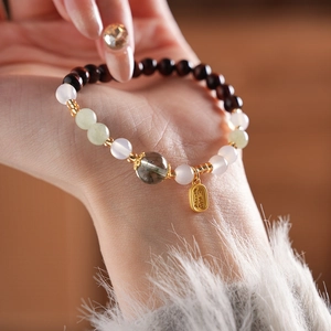 Detailed shot of green phantom crystal and tiger eye bead bracelet with a lucky gold charm