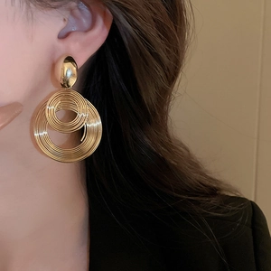 Detail shot of a model wearing layered geometric spiral gold-tone statement drop earrings