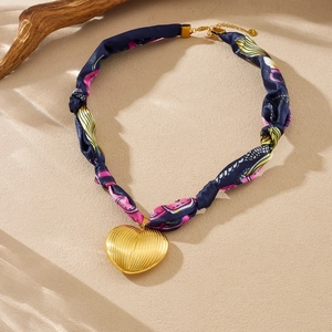 Detail of a gold heart pendant on a navy blue floral silk ribbon chain necklace