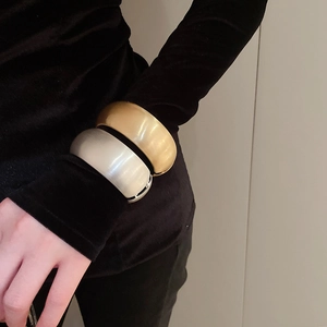 Detail of wide matte gold and brushed silver oval bangles worn over a black sleeve