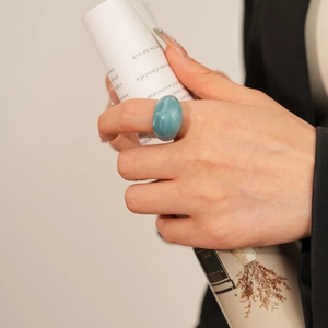 Gros plan sur une large bague ovale en résine bleu lagon portée par un mannequin chic