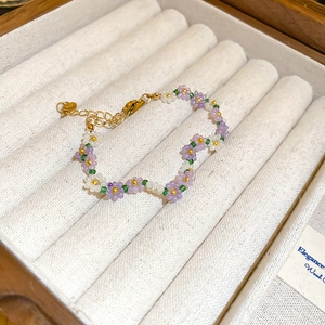Detailed view of handmade beaded flower bracelet in purple and white inside a jewelry box