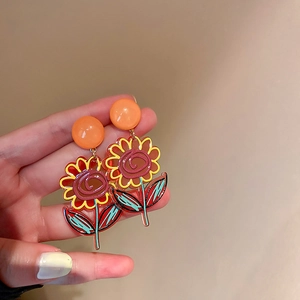 Gros plan de boucles d'oreilles tournesol en acrylique avec feuilles vertes à la main